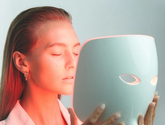 care-light-red-mask-led Una donna sul suo letto tocca con una piuma la sua pelle liscia e priva di peli grazie al trattamento laser effettuato presso la Novaskin Clinic di Bruxelles.